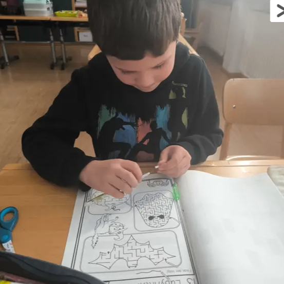 Ein Junge malt eine Labyrinth auf einem Papier mit einem grünen Stift, sitzt an einem Tisch.