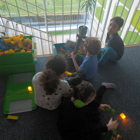 Vier Kinder sitzen auf dem Boden und bauen mit bunten Bauklöcken. Sie sind von Aufbewahrungsboxen umgeben, die mit Bauklöcken gefüllt sind.