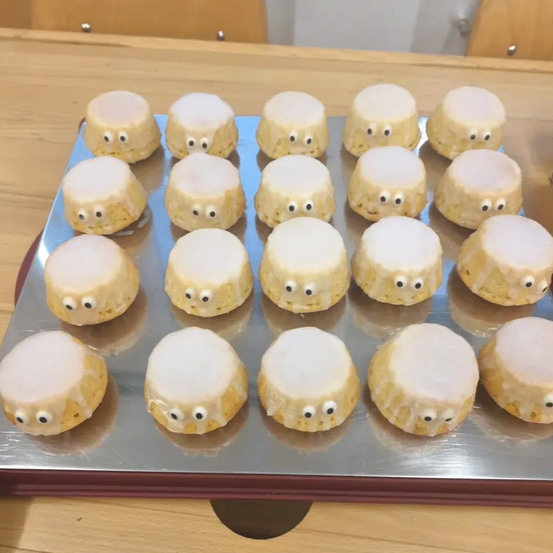 Ein Tablett mit kleinen, runden, weiß glasierten Keksen mit schwarzen Augen, die in einem Raster auf einem Holztisch angeordnet sind.