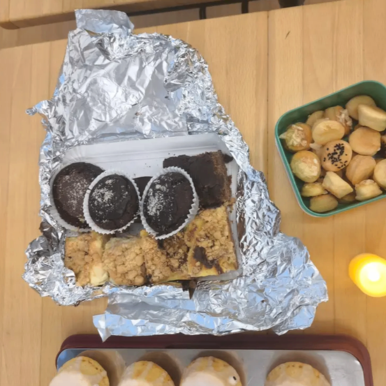 Ein Tablett mit in Folie eingewickelten Schokoladenüberzogenen Desserts steht auf einem Holztisch, begleitet von einer Schüssel mit frittierten Bällen. Eine kleine brennende Kerze sorgt für Wärme.