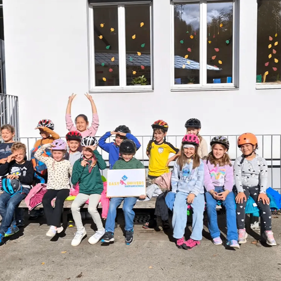 Kinder in Helmen posieren für ein Foto vor einem Gebäude mit Herbstdekorationen an den Fenstern.