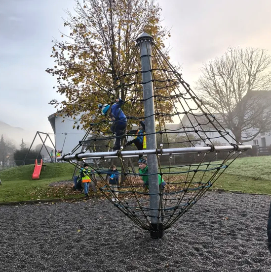 Ein Spielplatz mit einer roten Rutsche und Kindern, die auf einer Metallstruktur mit Netz klettern.