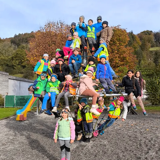 Eine Gruppe von Kindern in Warnwesten posiert für ein Foto auf einem Spielplatz. Sie stehen und sitzen auf einem Klettergerüst.