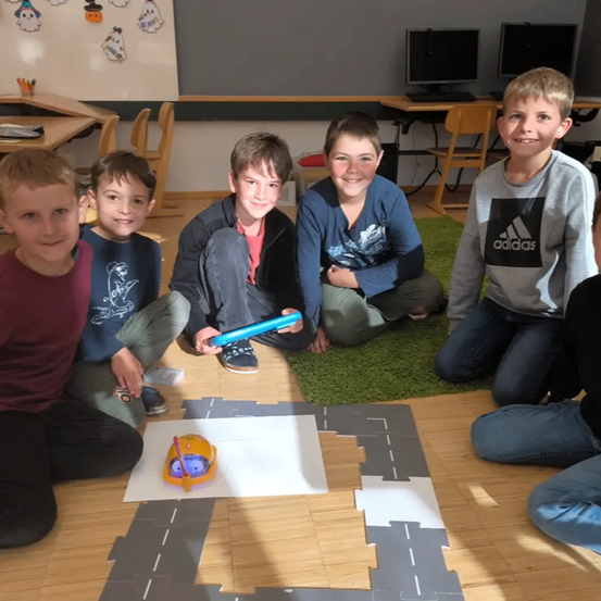 Fünf Jungen sitzen auf dem Boden mit einem Papierweg und einem Spielzeugauto vor ihnen. Sie lächeln und scheinen ein Spiel zu spielen.