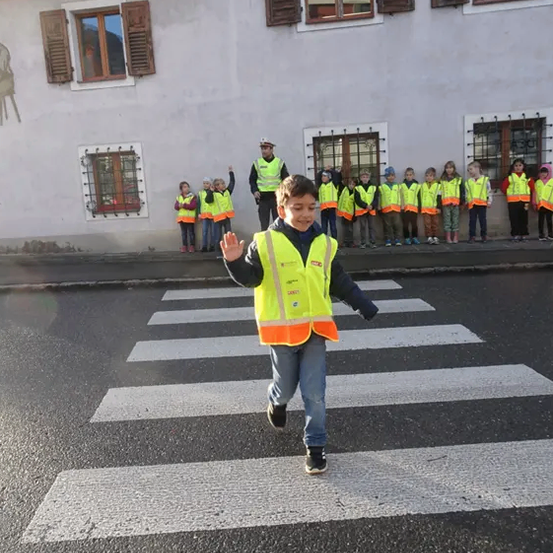 Ein Junge in einer gelben Sicherheitsweste geht mit anderen Kindern in Sicherheitswesten hinter ihm über einen Zebrastreifen.