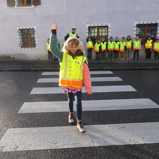 Ein Mädchen in einer reflektierenden Weste läuft mit einer Reihe von Kindern in gelben Westen hinter ihr über eine Zebrastreifen.