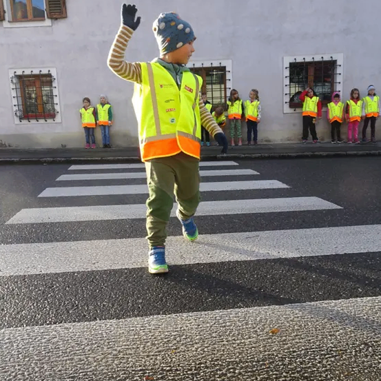 Ein Junge in einer gelben Weste dirigiert den Verkehr an einer Fußgängerüberführung, mit einer Reihe von Kindern in gelben Westen dahinter.