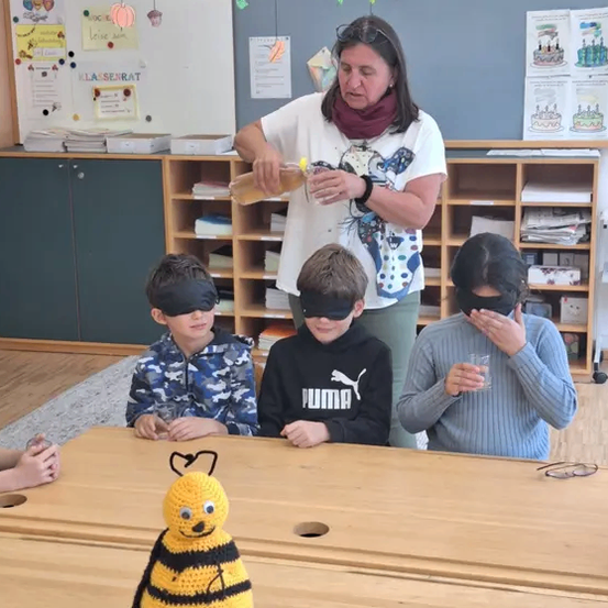Eine Frau gießt Saft in ein Glas für verbundene Kinder an einem Tisch mit einer gehäkelt Biene.
