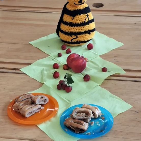 Ein Holztisch hat ein Bienen-Plüschtier, zwei Teller mit Gebäck und roten Kirschen auf grünen Servietten.