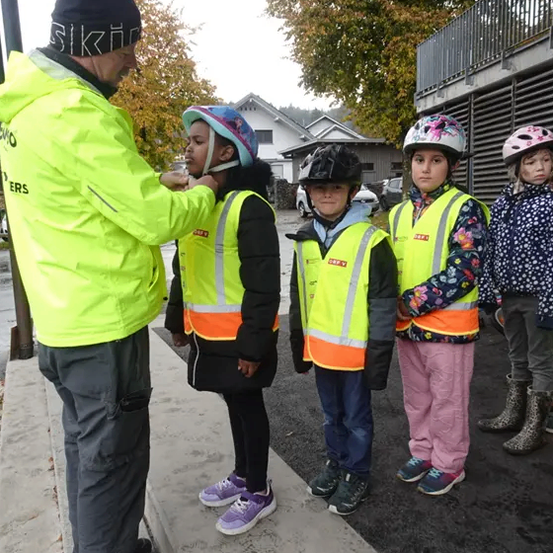 Ein Mann hilft einem jungen Mädchen mit ihrem Helm. Drei weitere Kinder, alle mit Sicherheitswesten, stehen hinter ihr.
