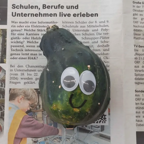 Ein Zeitungsausschnitt zeigt einen Kürbis mit Augen und einem Lächeln. Darunter arbeitet ein Kind an einem elektronischen Projekt.