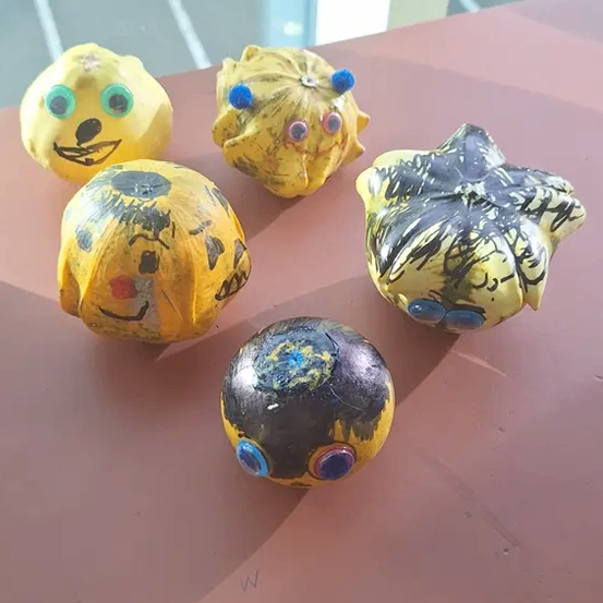 Fünf kleine gelbe und schwarze bemalte Objekte sind auf einer braunen Oberfläche angeordnet. Sie sind kugelförmig mit gemalten Augen und Gesichtern. Eines hat eine blaue Kugel obenauf.