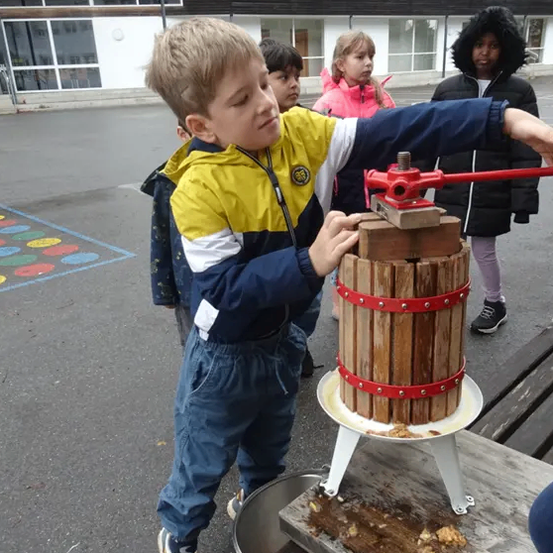 Ein junger Junge benutzt im Freien eine Holzpresse, um Saft zu pressen, während andere Kinder zusehen.