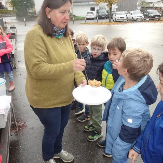 Eine Frau serviert Kindern in einer Reihe draußen in einer Stadt Essen auf einem Teller.