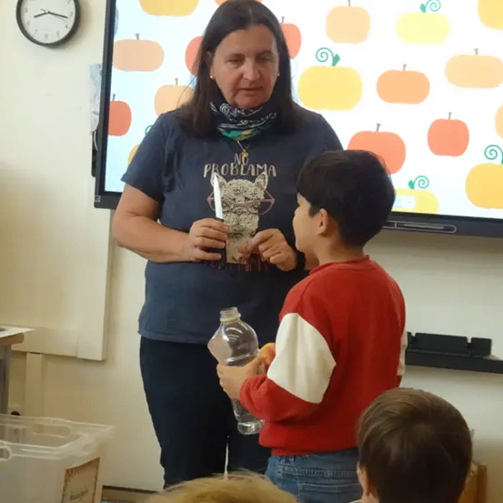 Eine Frau steht mit einem Jungen, der eine Flasche in der Hand hält, in einem Klassenzimmer mit einer Kürbistapete.