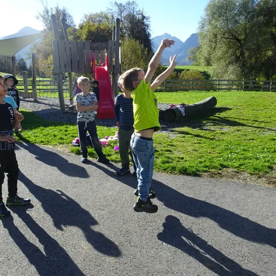 Ein Junge in einem grünen Shirt fängt einen Basketball im Freien in der Nähe eines Spielplatzes, während andere zuschauen.