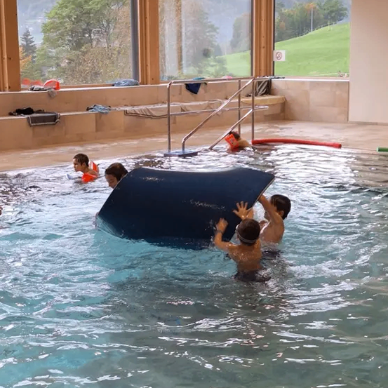 Mehrere Kinder spielen in einem Innenpool. Ein Kind klettert auf einen blauen Wasserrutsche.