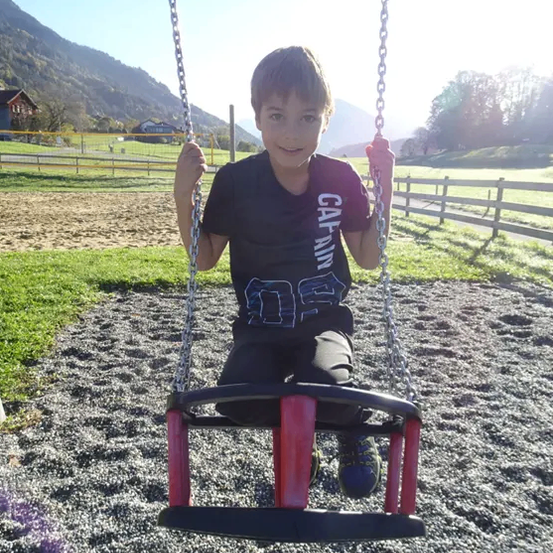 Ein junger Junge in einem schwarzen Shirt mit dem Wort 'Calvin' schwingt sich auf einer Schaukel im Park.