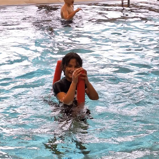 Ein kleiner Junge und ein junges Mädchen schwimmen in einem Pool mit roten Schwimmhilfen. Das Mädchen lächelt und posiert für ein Foto.