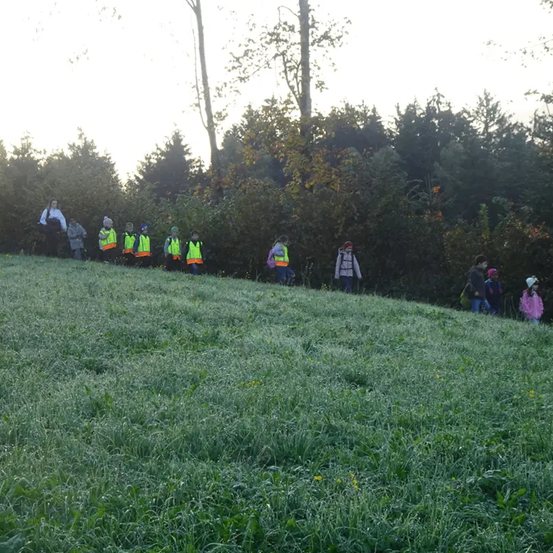 Eine Gruppe von Kindern und Erwachsenen in neonfarbenen Westen geht auf einem Grashügel unter klarem Himmel.