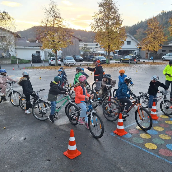 Eine Gruppe von Kindern übt das Fahrradfahren auf einem Parkplatz mit Verkehrskegeln.