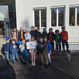 Eine Gruppe von Kindern mit Helmen steht vor einem Schulgebäude und posiert für ein Foto mit einem Schild, das 'Easy Drivers' besagt.