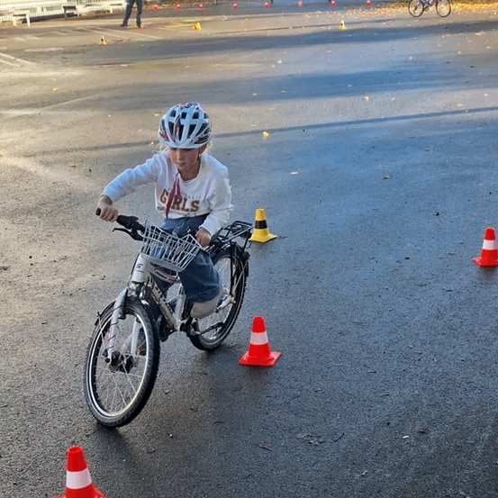 Ein Kind fährt mit einem Fahrrad durch einen Parcours mit Kegel auf einer asphaltierten Straße und trägt einen Helm.