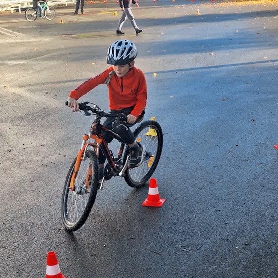 Ein Junge fährt ein Fahrrad durch einen Hindernisparcours mit Verkehrskegel und trägt einen Helm.