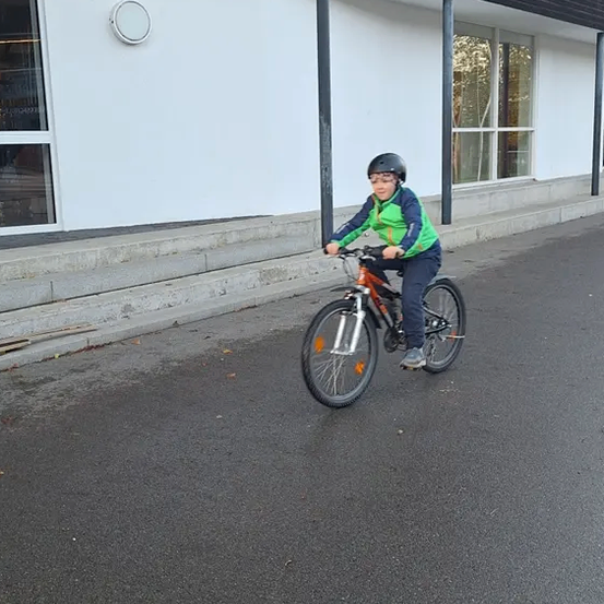 Ein Kind fährt mit dem Fahrrad die Straße hinunter vor einem Gebäude mit einer Glaswand.