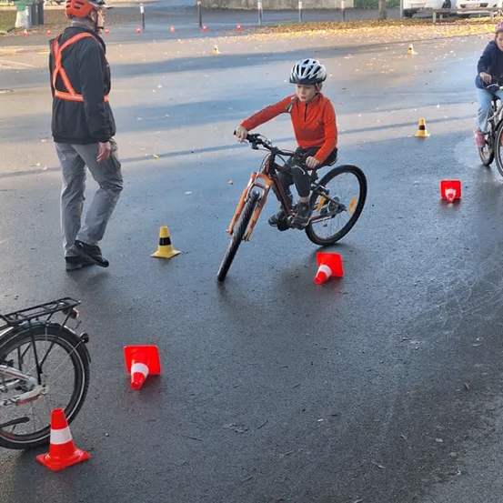 Ein junger Junge übt das Radfahren mit einem Erwachsenen auf einem Parkplatz mit Verkehrskegeln.