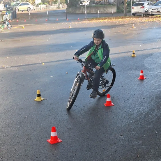 Ein junger Junge mit Helm fährt ein Fahrrad durch eine Hindernisstrecke mit Verkehrskegeln.