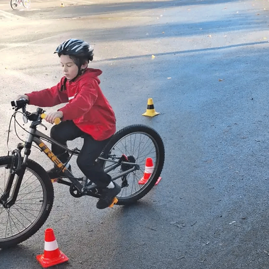 Ein junger Junge navigiert mit einem Fahrrad durch einen Hindernisparcours mit Verkehrskegel auf einer nassen Straße.