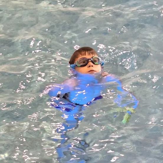Ein junger Junge in Schwimmbrille und blauem Neoprenanzug schwimmt im Pool.