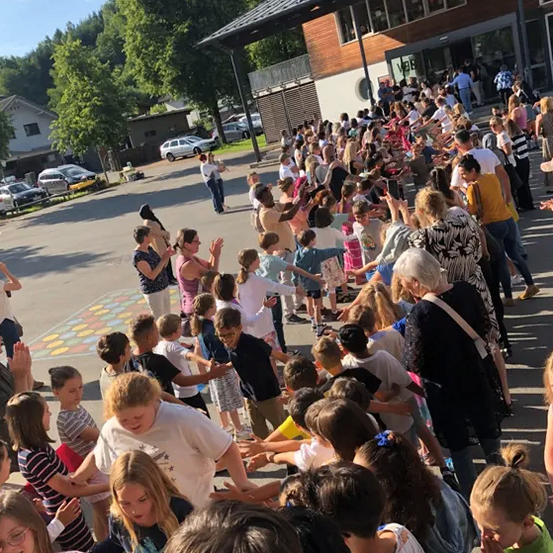 Eine große Menschenmenge, darunter Kinder, Erwachsene und Senioren, versammelt sich vor einem Gebäude, möglicherweise für eine Veranstaltung, unter klarem Himmel.
