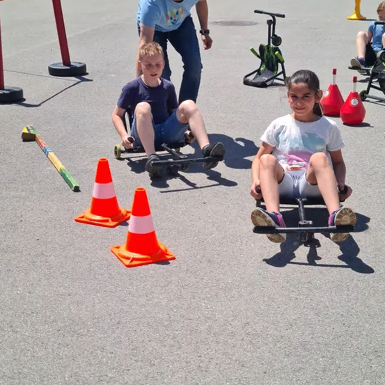 Ein Mann und zwei Kinder fahren auf Go-Karts um orangefarbene Verkehrskegel auf einer gepflasterten Fläche.