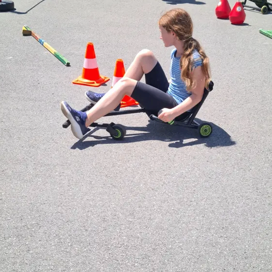 Ein Mädchen sitzt auf einem Roller auf dem Bürgersteig mit Verkehrskegeln und anderen Gegenständen um sie herum.