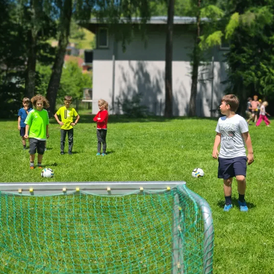 Eine Gruppe von Kindern spielt Fußball auf einem Rasenfeld, wobei ein Junge nach oben schaut und ein anderer einen Fußball hält.