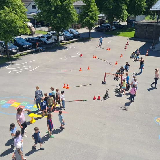 Ein Parkplatz mit Kindern, die eine Hindernisbahn spielen. Sie laufen um Kegel und eine Frau führt.