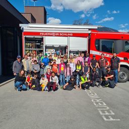 Eine Gruppe von Kindern und Erwachsenen posiert für ein Foto vor einem roten Feuerwehrauto in Schlins, Österreich.