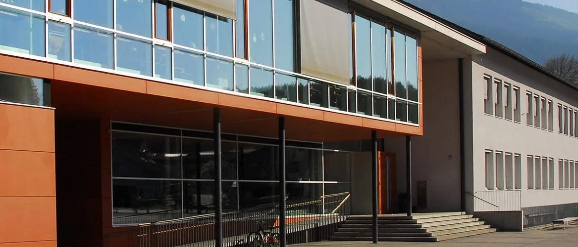 Ein modernes Gebäude mit Glaswänden und Fenstern, einer Metallbrüstung und einem Fahrrad vor dem Gebäude.