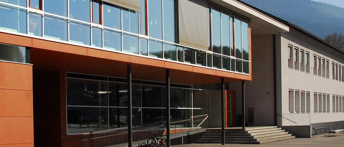 Ein modernes Gebäude mit Glaswänden und Fenstern, einer Metallbrüstung und einem Fahrrad vor dem Gebäude.