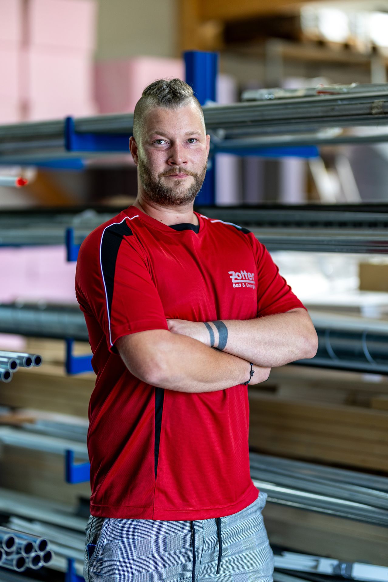 Ein Mann in einem roten Shirt mit Zotter Logo steht mit verschränkten Armen in einer Fabrik.