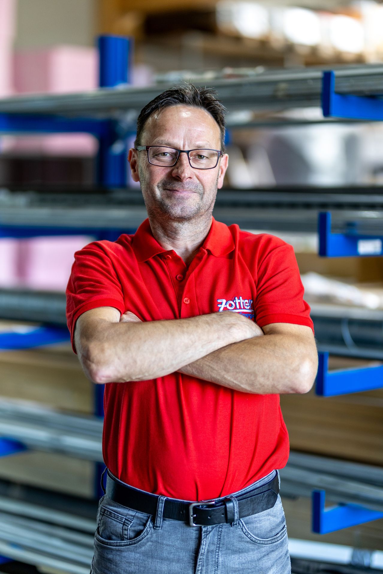 Ein Mann mit Brille und einem roten Shirt mit dem Wort Zotter steht mit verschränkten Armen in einem Lager.