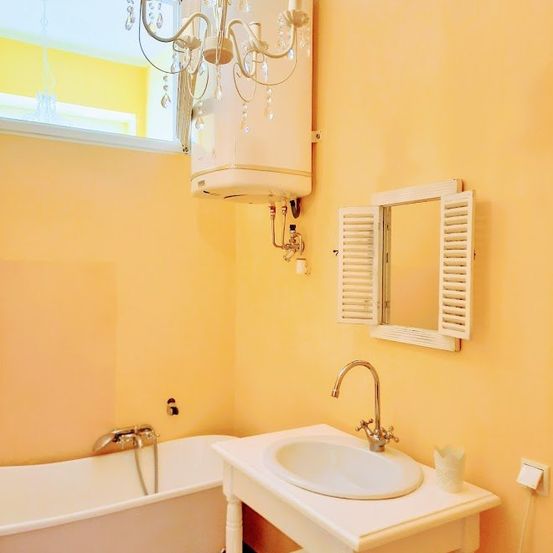 Ein Badezimmer mit gelben Wänden, einer weißen Badewanne, einer Kronleuchter, einem Waschbecken und einem Spiegel mit weißen Fensterläden.