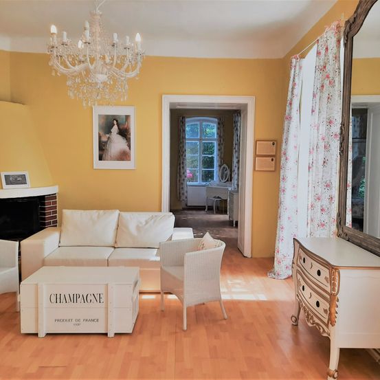 Ein Wohnzimmer mit gelben Wänden, einem weißen Sofa, einem weißen Stuhl und einem weißen Couchtisch mit dem Wort Champagne darauf. Eine Kristallleuchte hängt von der Decke.
