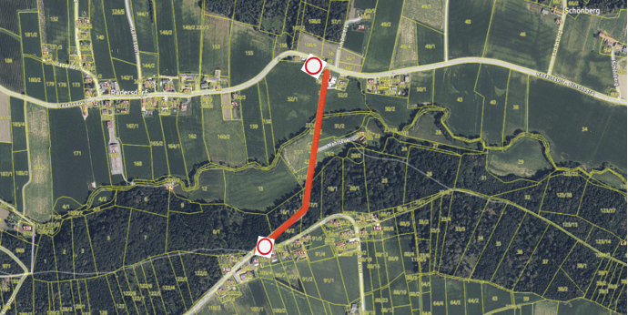 Eine Luftaufnahme zeigt ein ländliches Gebiet mit durchnummerierten Grundstücken. Eine rote Linie hebt einen Weg hervor, der von oben nach unten führt, mit roten Kreisen, die bestimmte Punkte markieren.