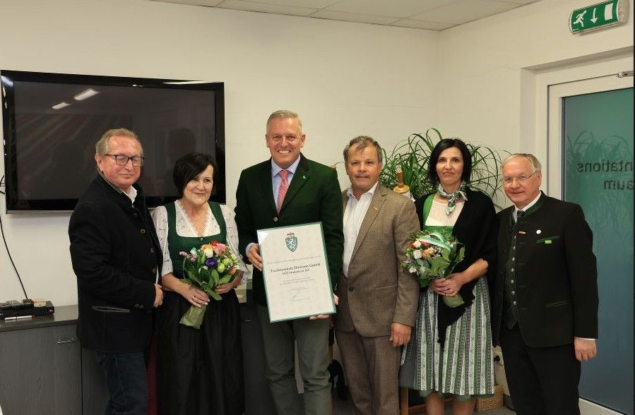 Eine Gruppe von Menschen posiert für ein Foto, hält ein Zertifikat und Blumensträuße und ist in traditioneller Kleidung gekleidet.