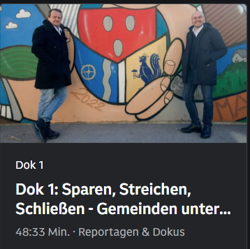Zwei Männer in dunklen Mänteln stehen neben einer farbenfrohen Wandmalerei, die eine Hand, einen Hahn und einen Schild darstellt. Der Text lautet 'Dok 1: Sparen, StreiChen, SchlieBen - Gemeinden unter...' und darunter '48:33 Min.: Reportagen & Dokus.'