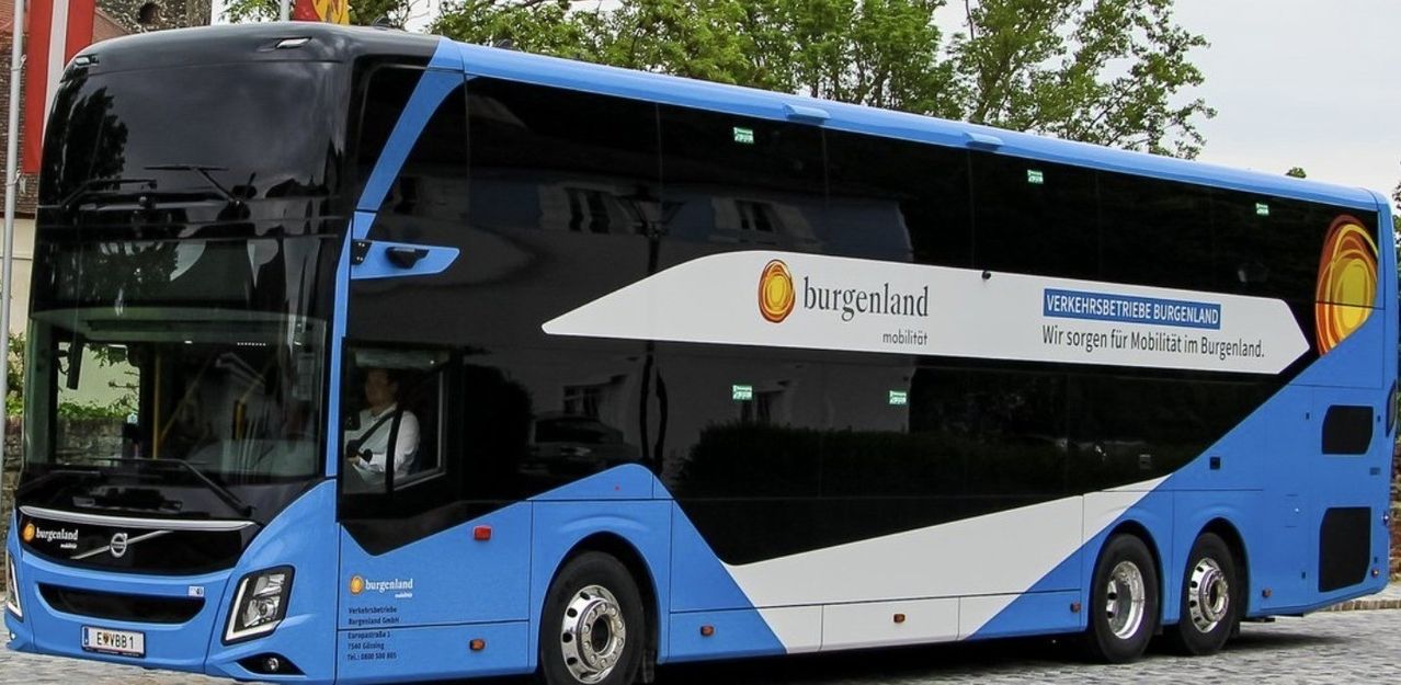 Ein blauer und weißer Bus mit 'burgenland' Logo steht vor einem Gebäude mit Bäumen im Hintergrund.