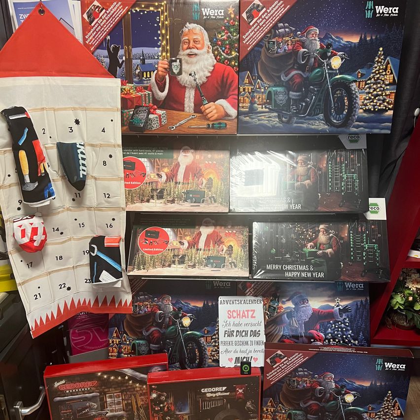 Eine Ausstellung von Weihnachtsdekorationen in einem Geschäft, darunter ein Weihnachtskalender mit dem Weihnachtsmann, eine Motorradszene und ein Schild mit der Aufschrift 'Frohe Weihnachten & ein glückliches neues Jahr'.